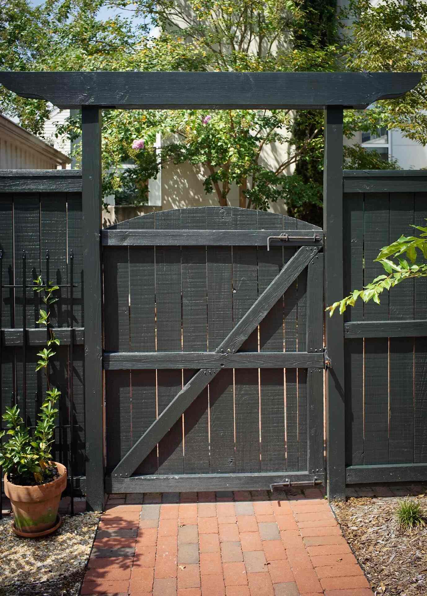 Backyard gate with pergola-style trim and red brick path in a custom home by Balding Design Build in Wilmington, NC