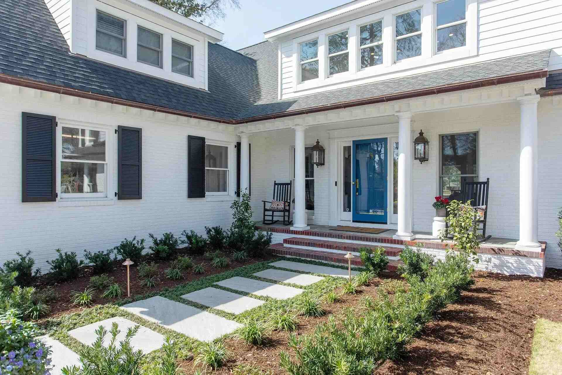 Front porch entryway of a Wilmington, NC custom home featuring columns, blue door, and lush landscaping by Balding Design Build